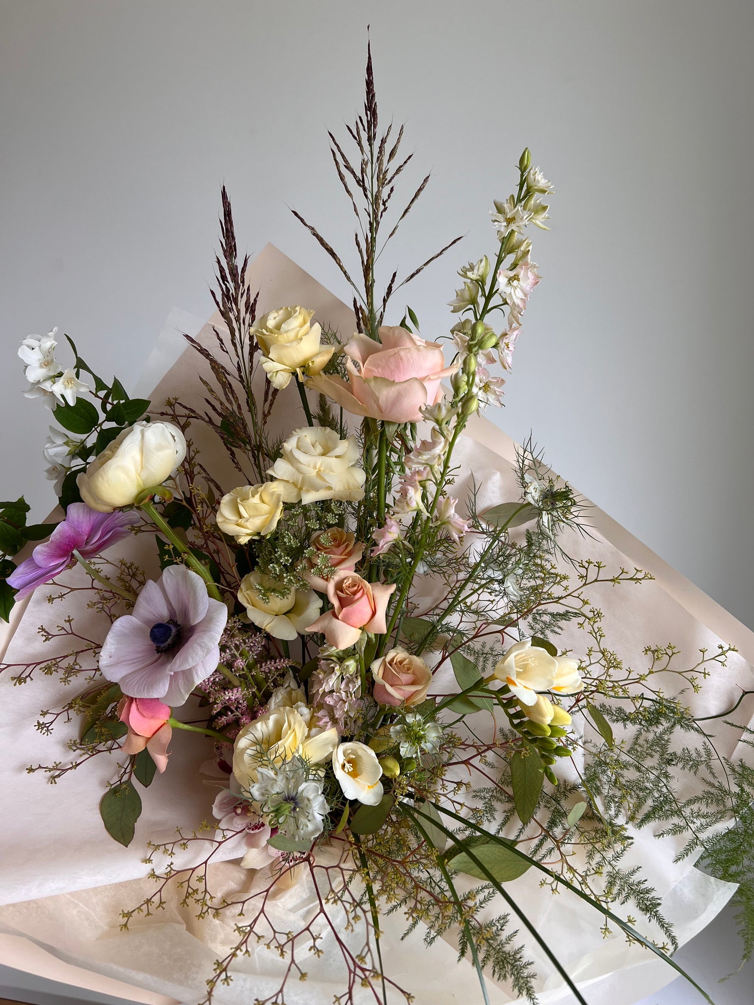 large hand tied bouquet is designed with statement flowers including local roses, peonies, anemone, and orchids or whatever is best in season
